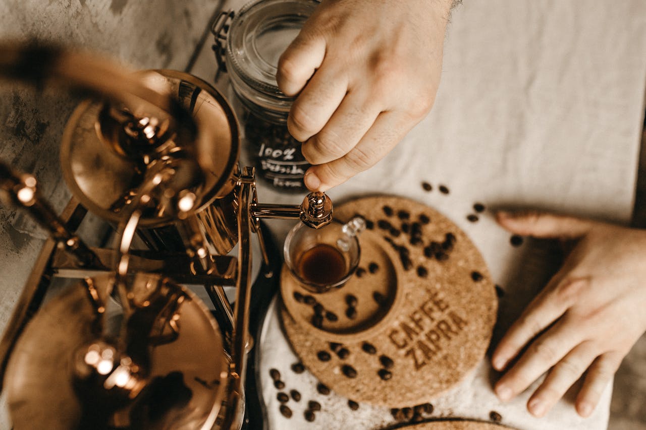 Close-up of hands brewing coffee with vintage copper espresso maker and coffee beans.