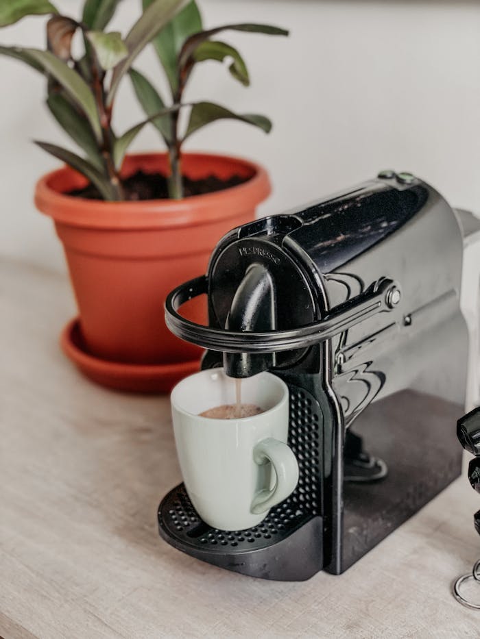 A modern coffee machine pours espresso into a white cup beside a potted plant, creating a cozy kitchen scene.