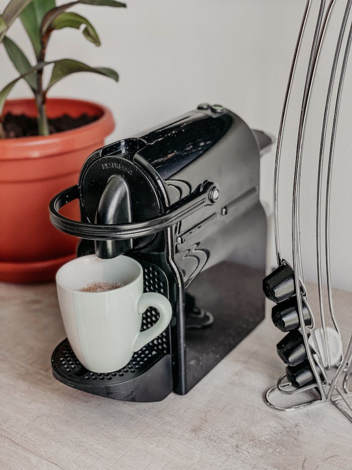 A modern black coffee maker with a white cup and a potted plant nearby, perfect for a cozy kitchen setup.