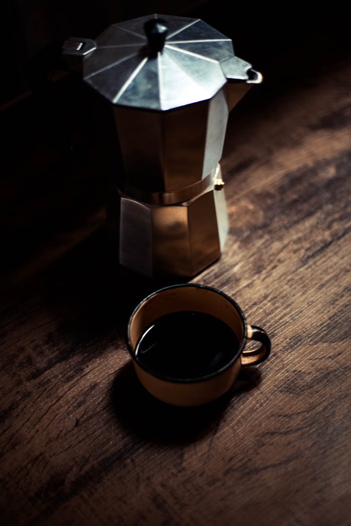 A rustic scene with a moka pot and cup of coffee on wooden table.