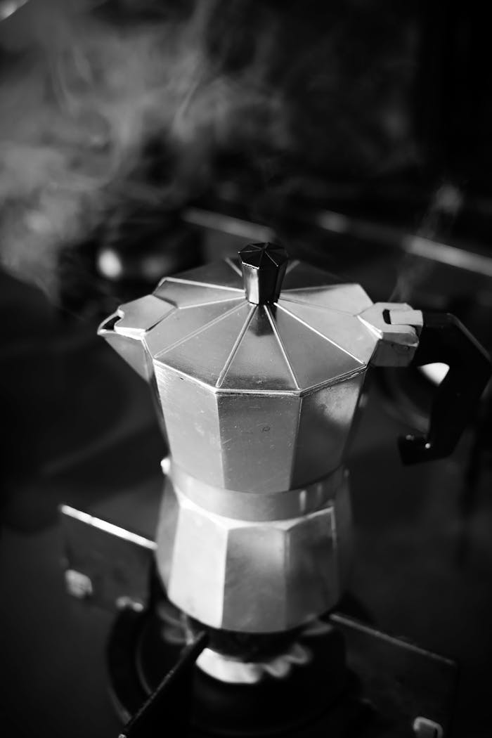 Steaming Moka pot on an active stove captured in a black and white aesthetic.