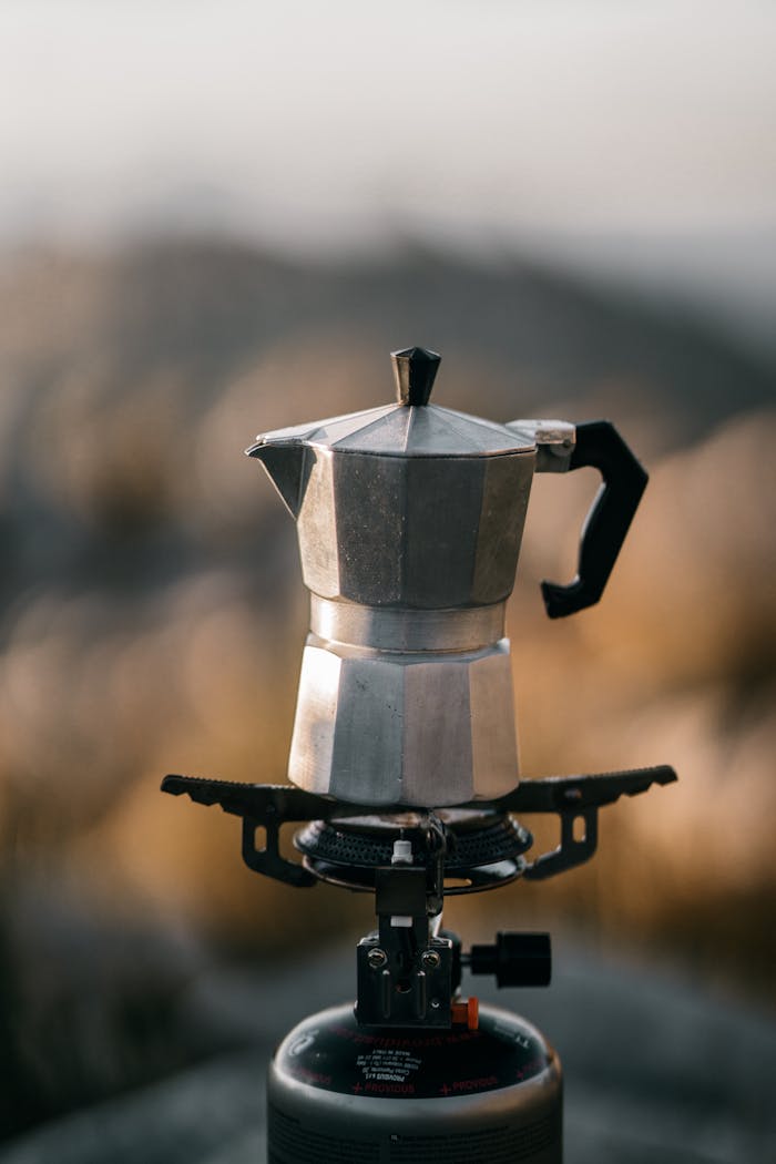 A moka pot makes coffee on a portable camping stove during an outdoor adventure.