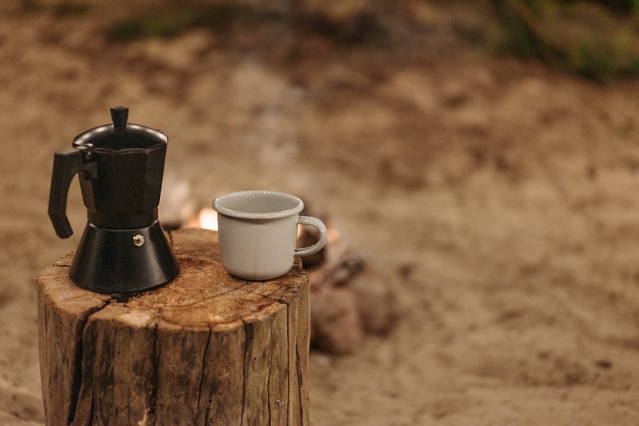 A moka pot and ceramic cup placed on a tree stump outdoors, perfect for a cozy coffee moment.